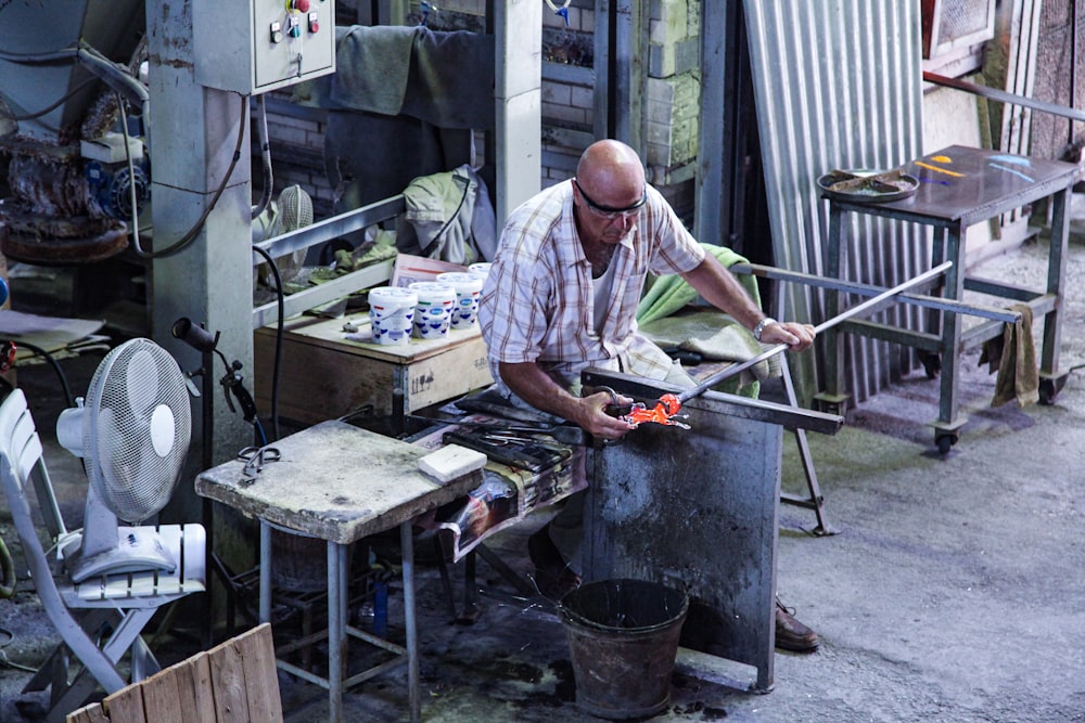 man in white and gray plaid button up shirt holding red and black power tool