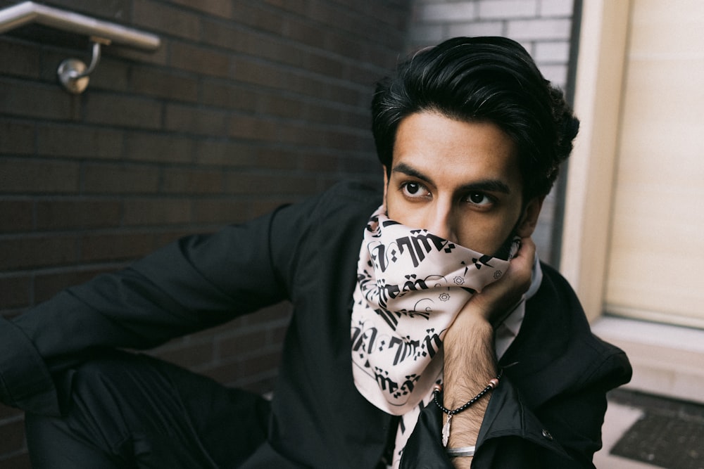 man in black leather jacket covering his face with white and black textile