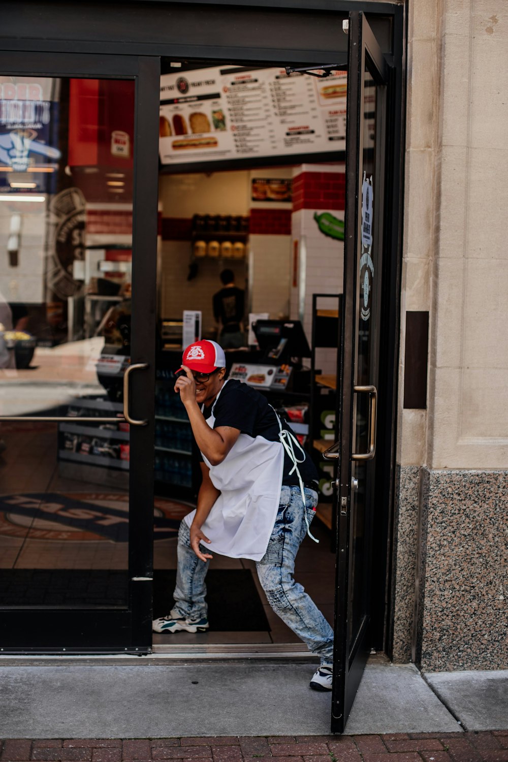 man in white t-shirt and blue denim jeans wearing red helmet leaning on glass window