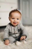 baby in gray sweater lying on white textile