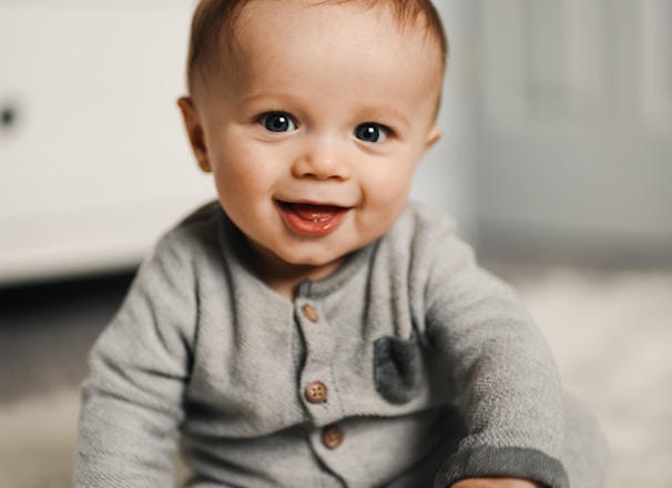 baby in gray sweater lying on white textile
