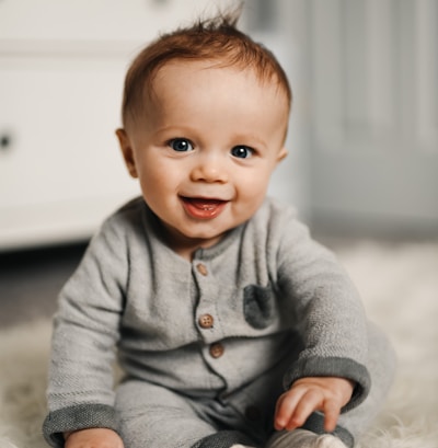 baby in gray sweater lying on white textile