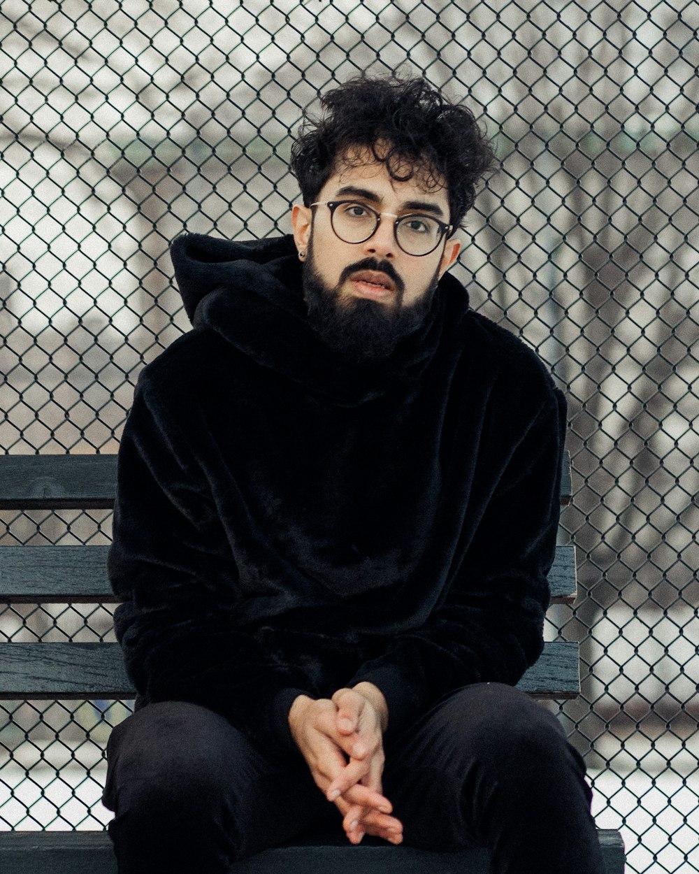 man in black hoodie sitting on gray metal fence