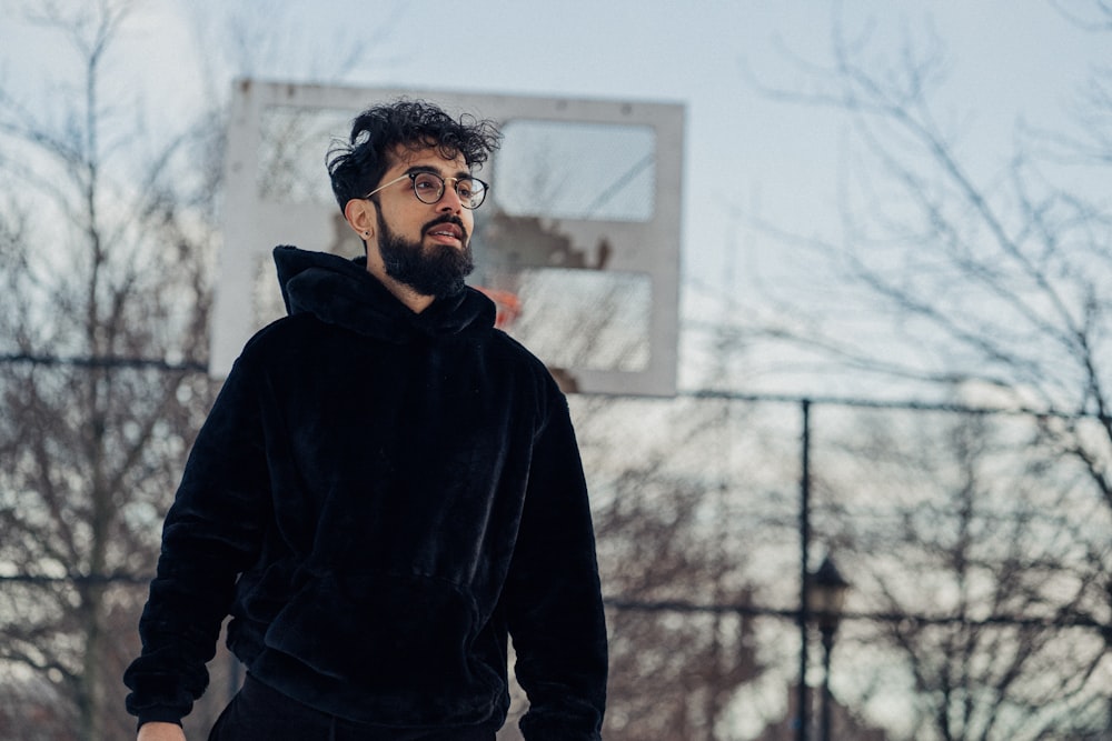 man in black hoodie standing near bare trees during daytime