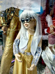 A shimmering gold cocktail dress showcased on a mannequin with soft spotlight highlighting its details.