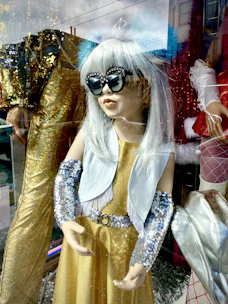 A shimmering gold cocktail dress showcased on a mannequin with soft spotlight highlighting its details.