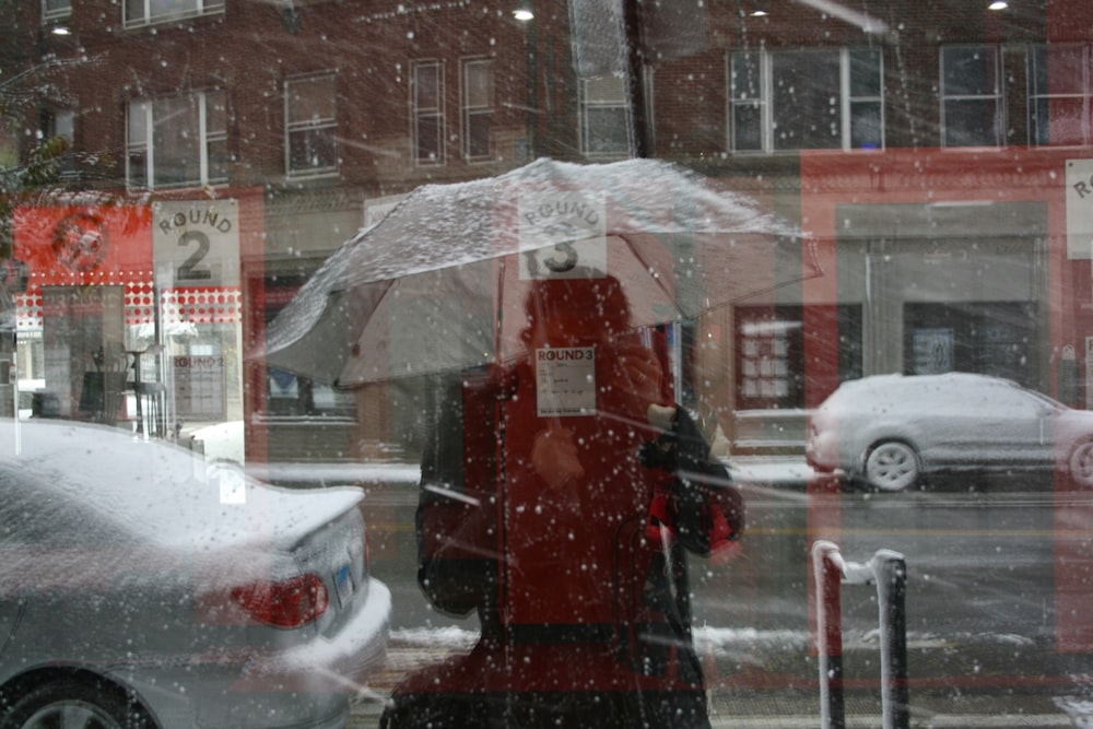 person in red coat holding umbrella standing on snow covered road during daytime