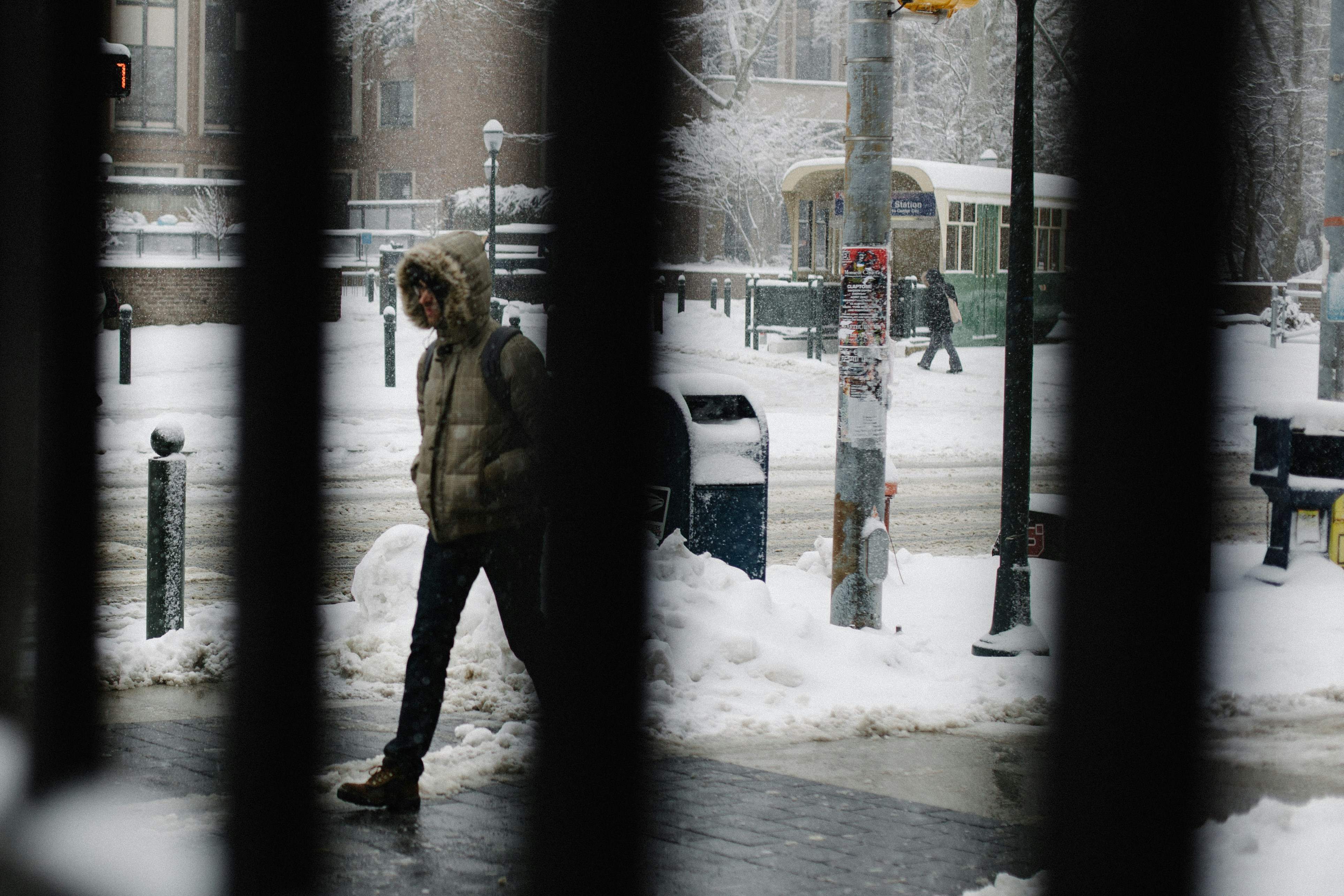 Student in hooded winter jacket walking on shoveled sidewalk on snowy college campus. 