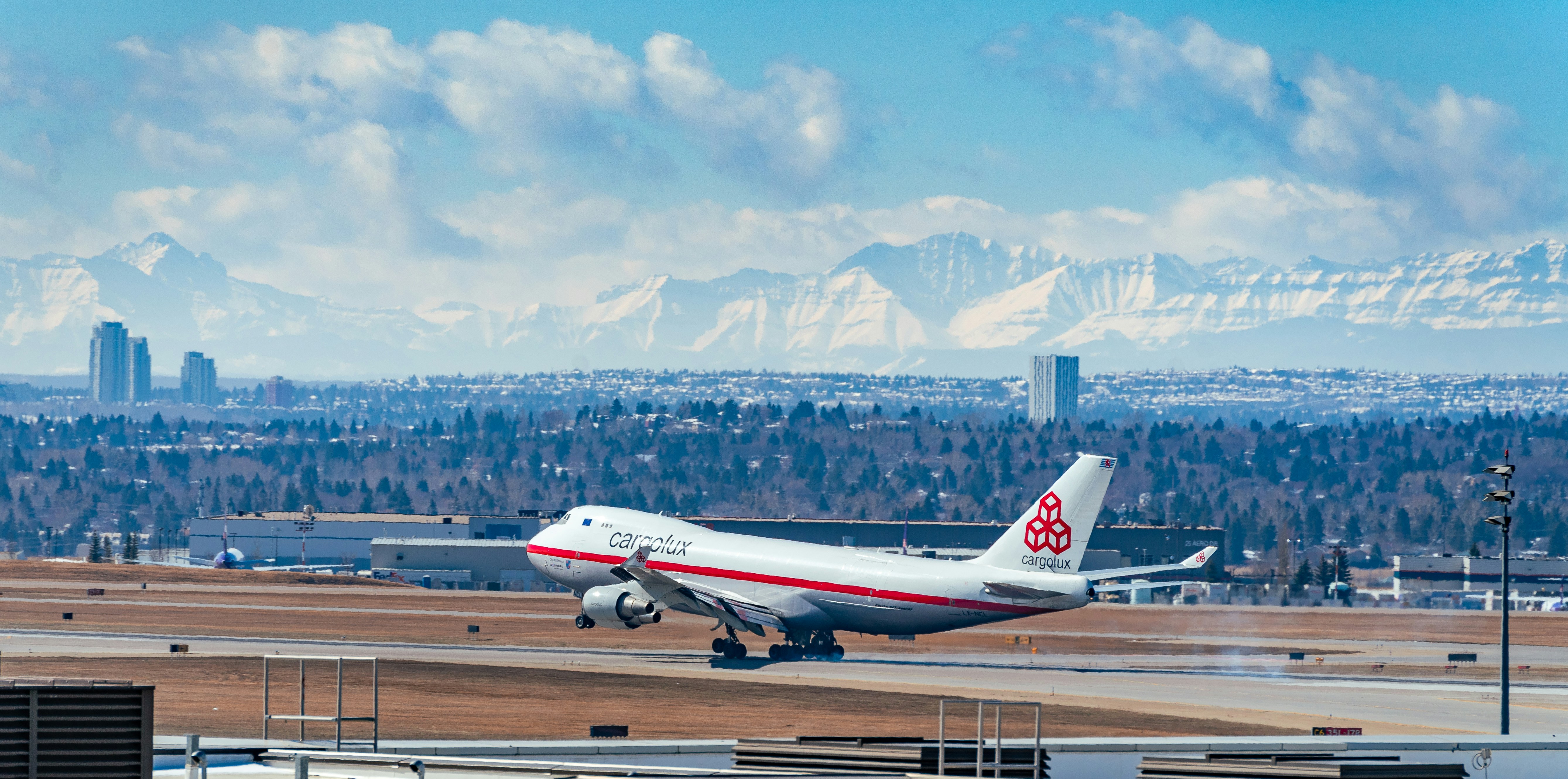 white and red passenger plane on airport during daytime, Cargolux 747 landing against a mountain backdrop.