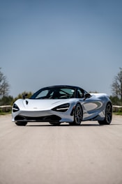 A sleek luxury car parked on a scenic highway under a clear blue sky.