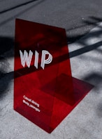A translucent red acrylic sign with the letters 'WIP' prominently displayed. Below, the text reads 'Casual dining @wip_seongsu'. The sign casts a shadow on the concrete pavement, which is partially lit by sunlight.