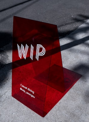 A translucent red acrylic sign with the letters 'WIP' prominently displayed. Below, the text reads 'Casual dining @wip_seongsu'. The sign casts a shadow on the concrete pavement, which is partially lit by sunlight.