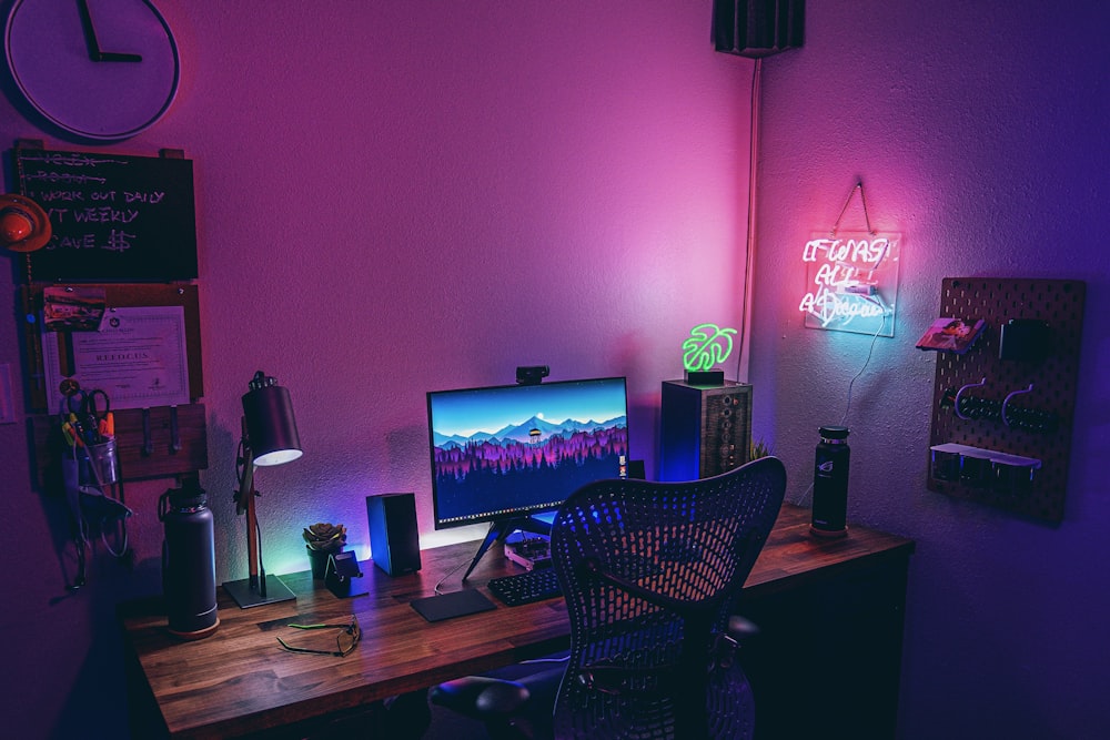 a desk with a computer and a neon sign
