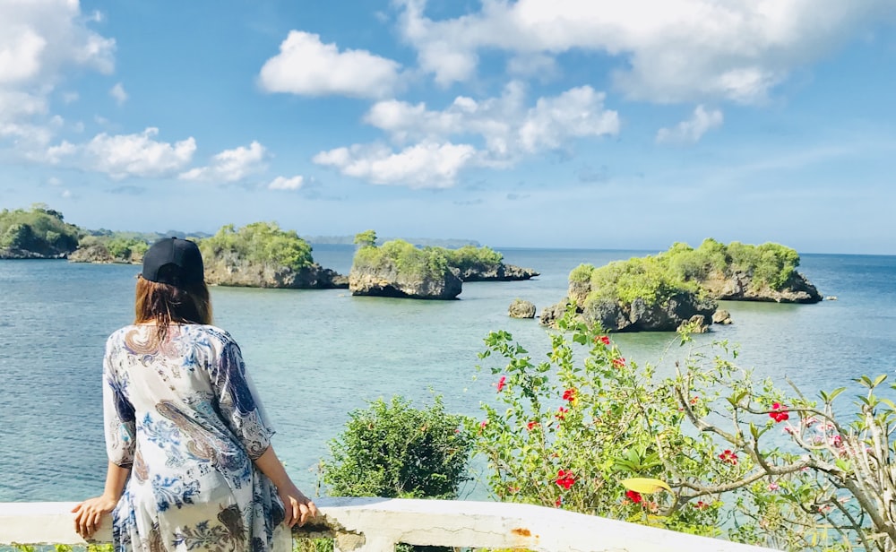 woman in white and blue floral dress sitting on white round table near body of water