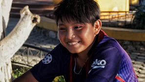 A young supporter smiling while wearing a Sportivo Luqueño shirt in a sunny park