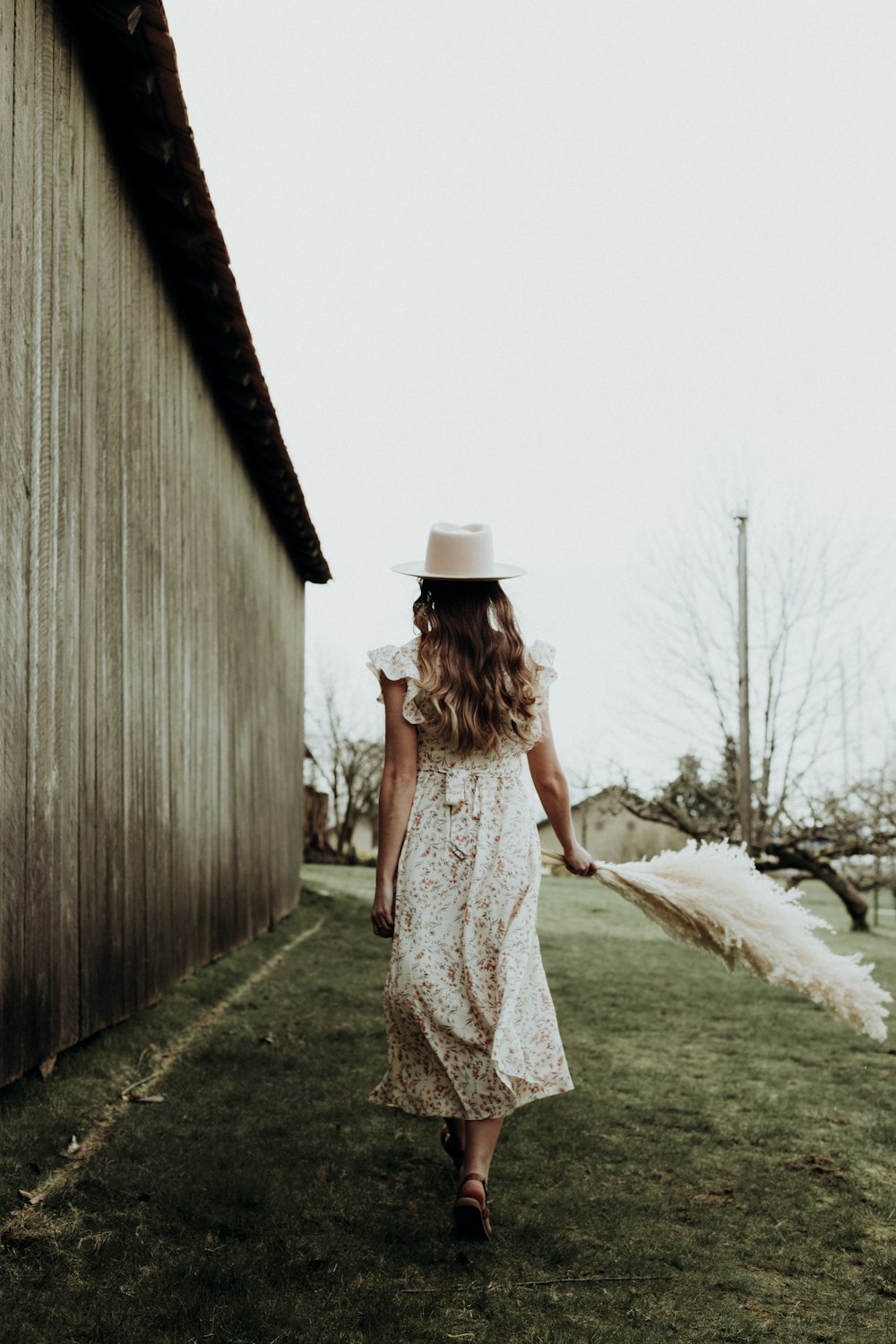donna in abito floreale bianco e marrone in piedi accanto alla staccionata di legno marrone durante il giorno