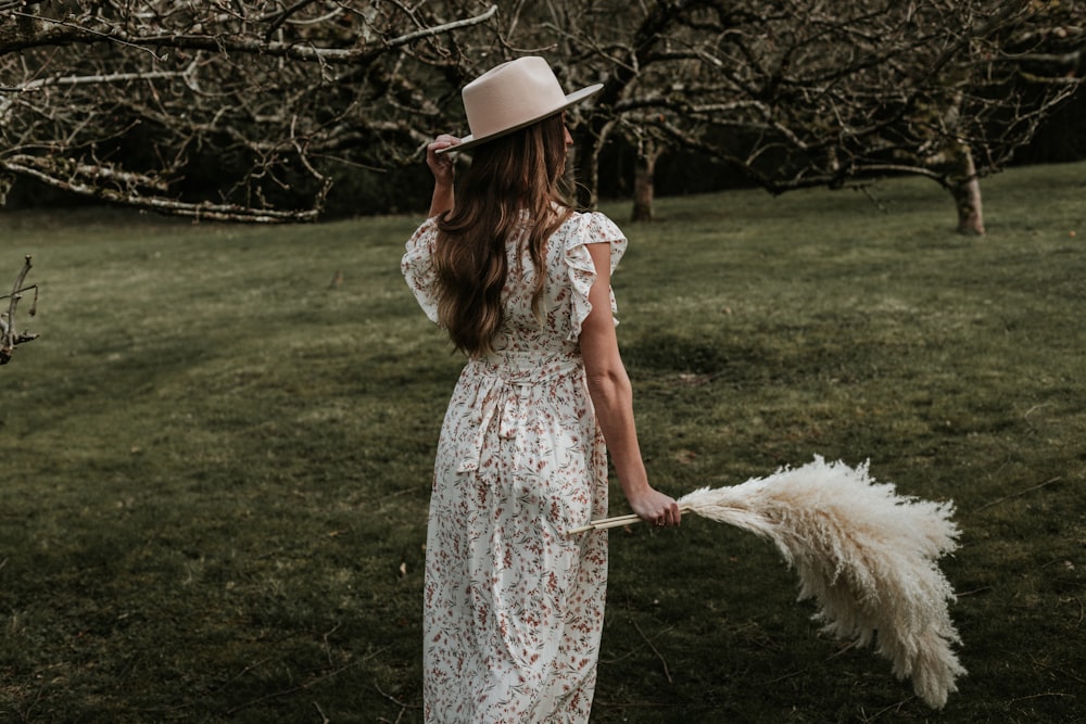 Mujer en vestido floral blanco sosteniendo paraguas blanco de pie en el campo de hierba verde durante el día