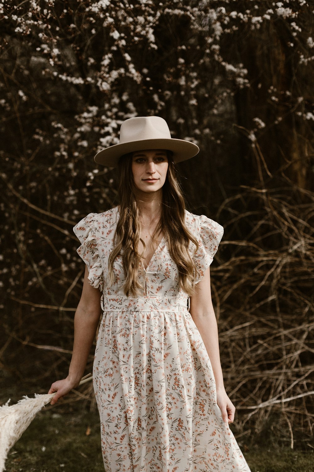 woman in white floral dress wearing brown hat standing in forest