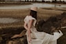 woman in white and red floral dress wearing brown hat sitting on brown rock during daytime