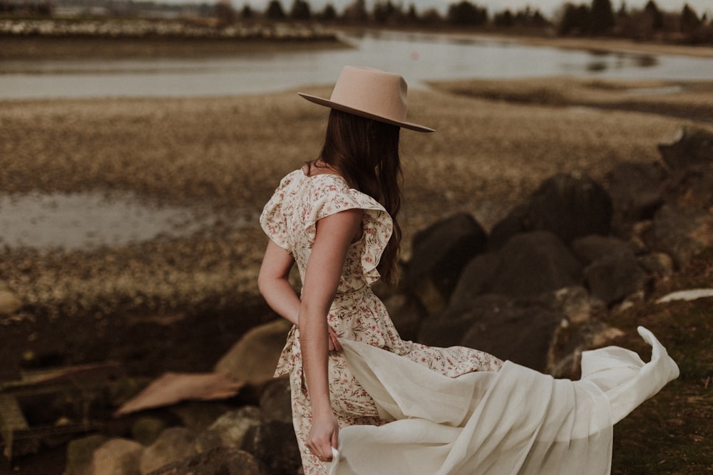 Mujer en vestido floral blanco y rojo con sombrero marrón sentada en roca marrón durante el día