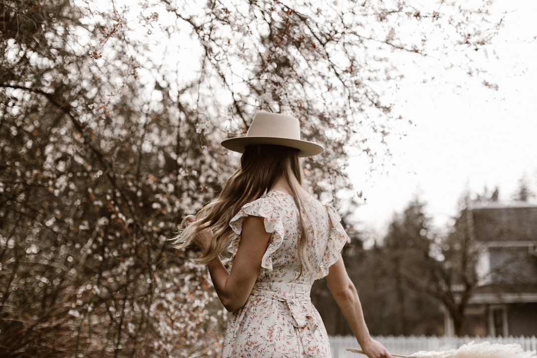 woman in white floral dress wearing white hat standing near trees during daytime