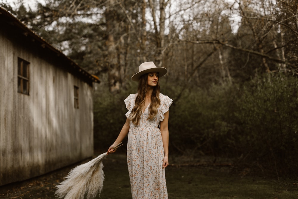 woman in white and brown floral dress wearing white hat standing near bare trees during daytime