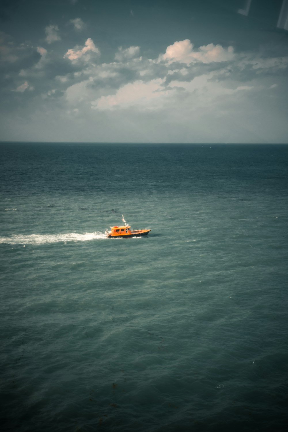 昼間の海上に浮かぶオレンジと白のボート