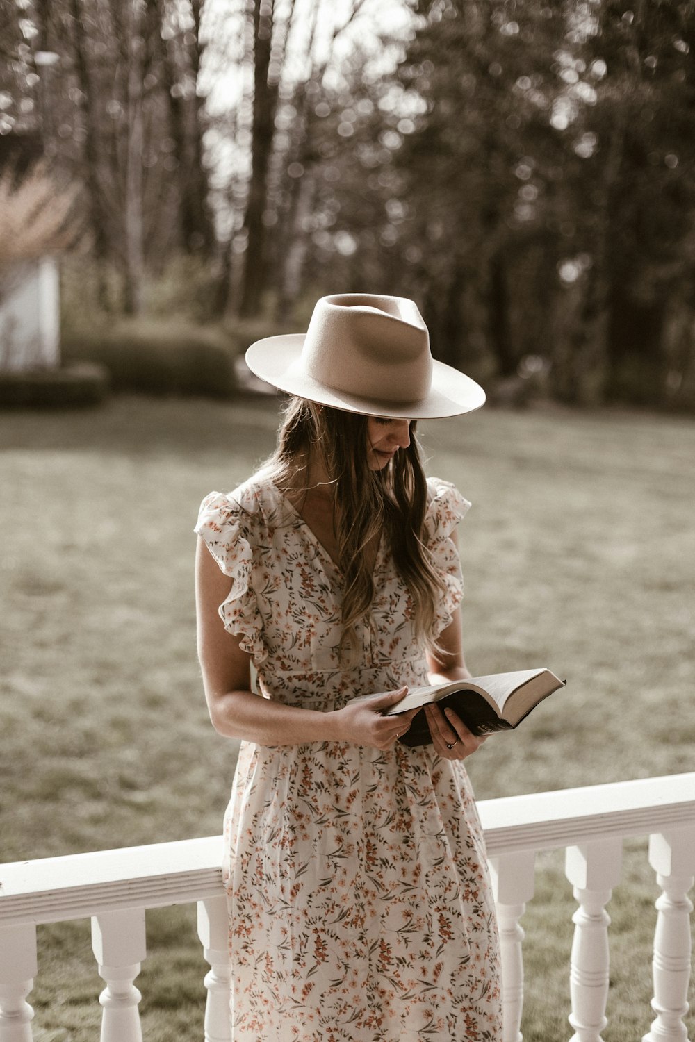 woman in white and brown floral dress wearing white hat standing on green grass field during