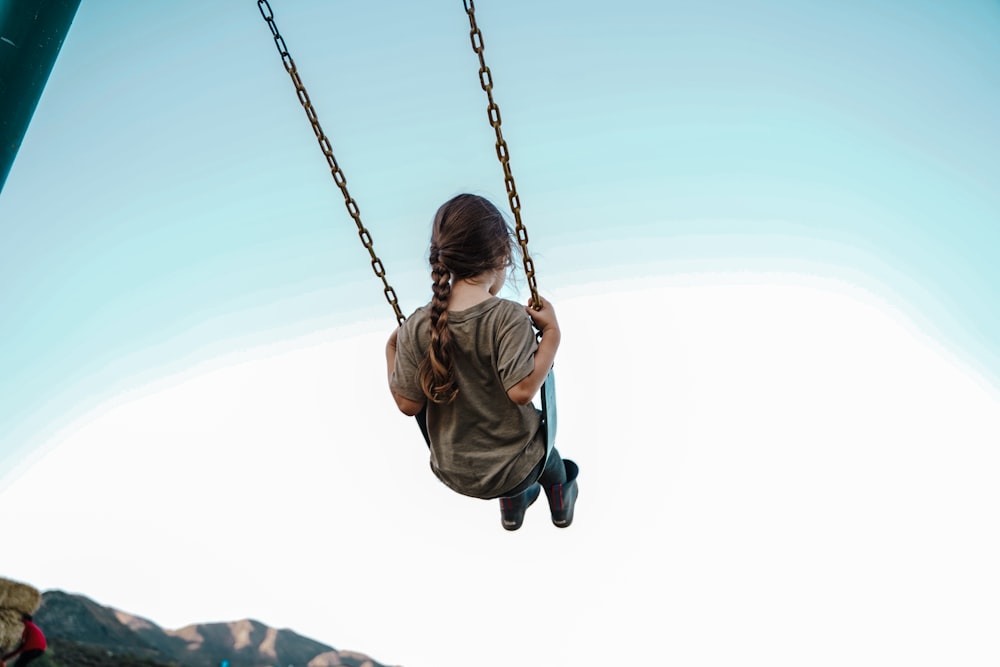 child in brown jacket sitting on swing during daytime