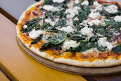 pizza with green leaves on brown wooden table