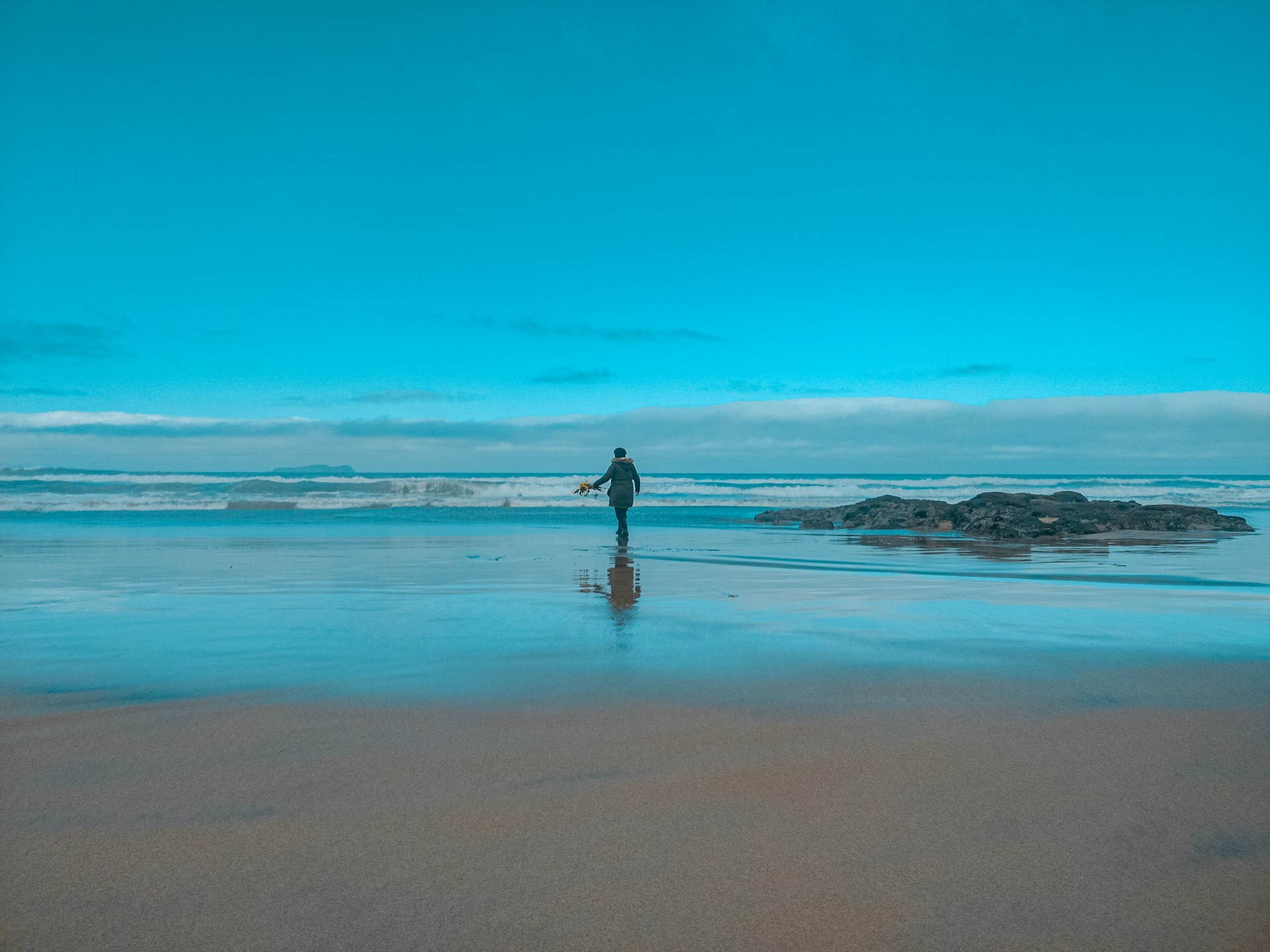 woman in black dress walking on beach during daytime