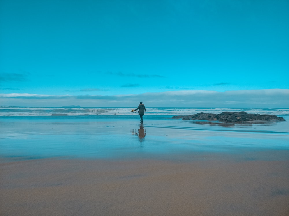 woman in black dress walking on beach during daytime