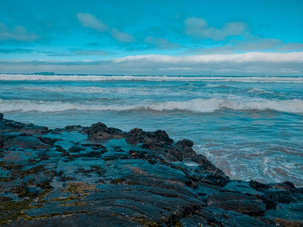 ocean waves crashing on rocks under blue sky during daytime