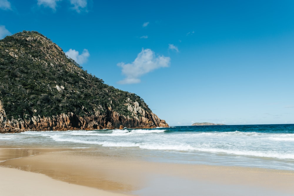 brown and green mountain beside sea under blue sky during daytime