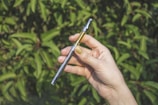 A hand holding a modern vape device with a smooth checkout screen blurred in the background.