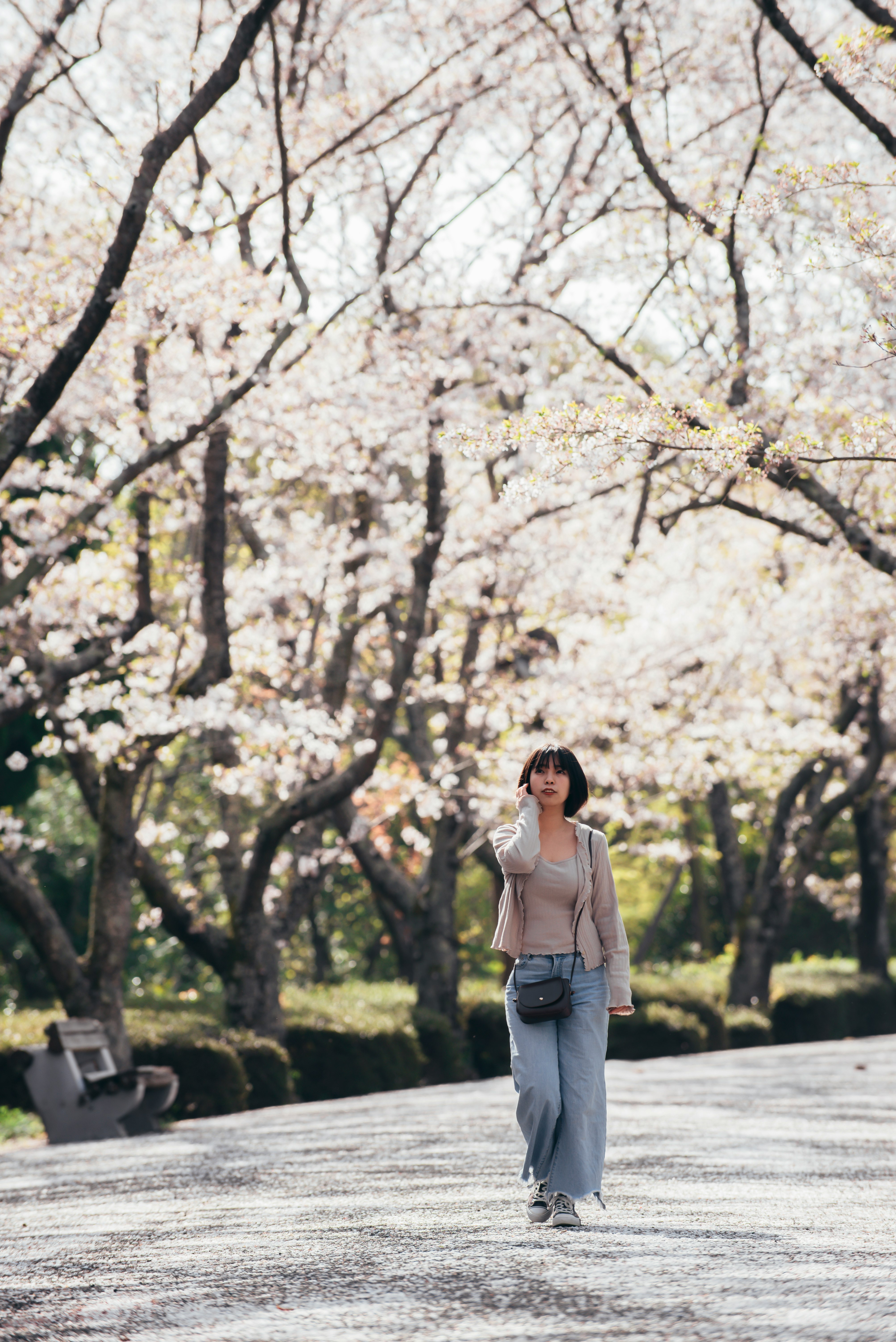 woman in white tank top and blue denim jeans standing on gray concrete pathway between trees