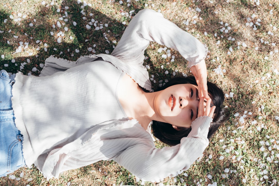 woman in white long sleeve shirt lying on green grass during daytime