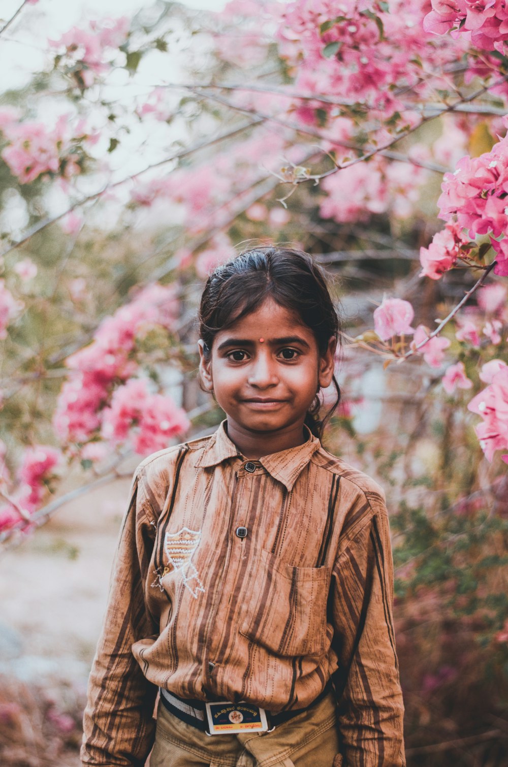 boy in brown button up shirt standing near pink flowers during daytime