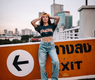 woman in black tank top and blue denim jeans standing on yellow and black road sign