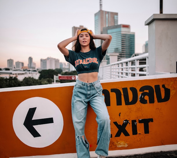 woman in black tank top and blue denim jeans standing on yellow and black road sign