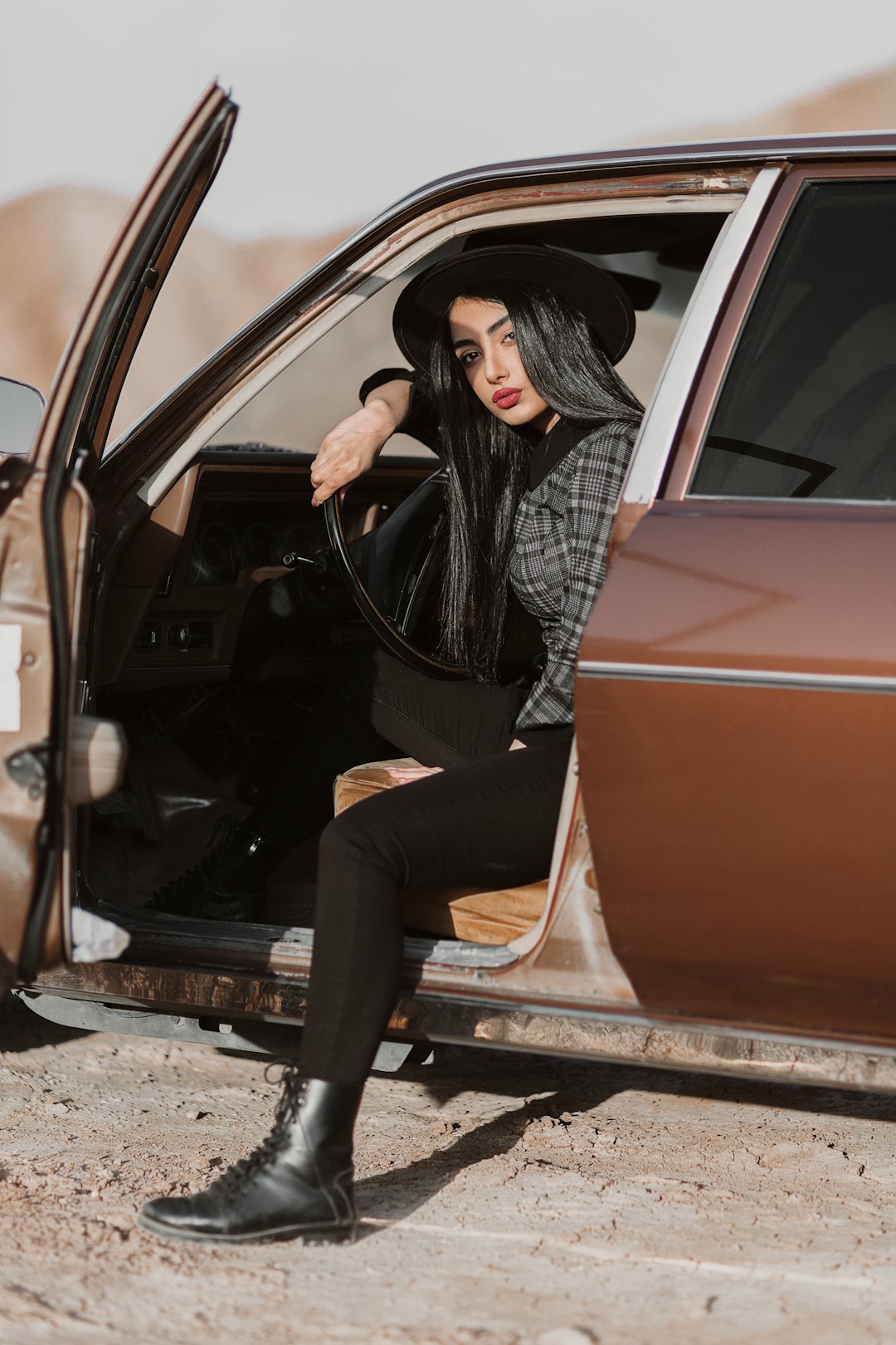 woman in black leather jacket and black pants sitting on car door during daytime