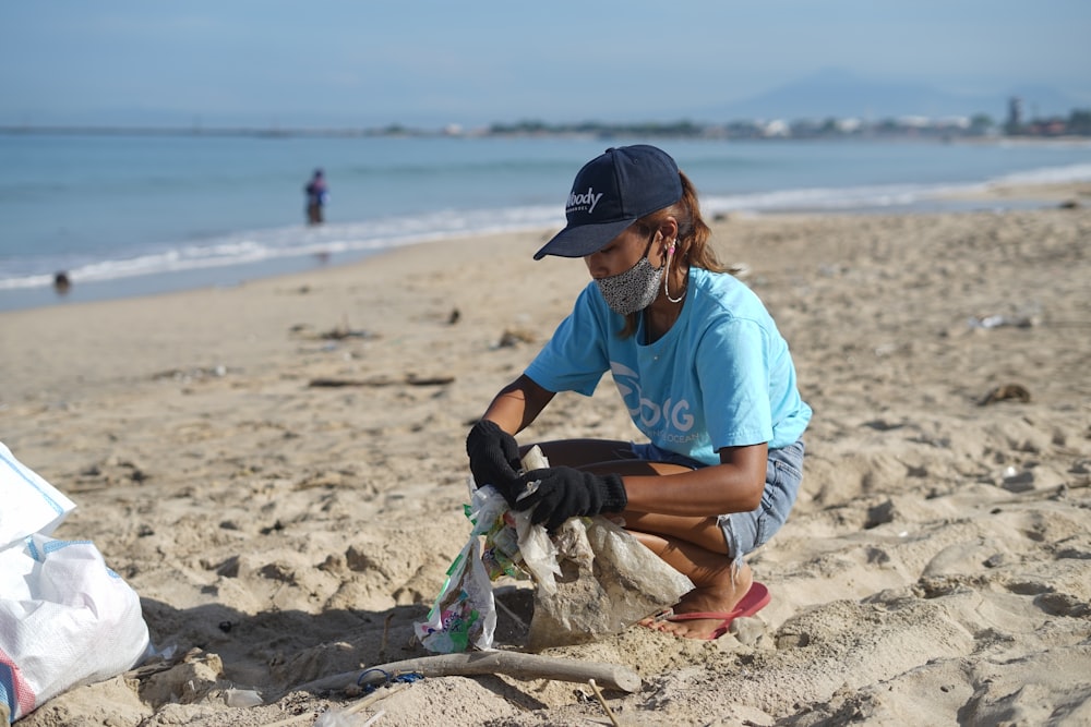 Homme en T-shirt bleu et casquette noire assis sur la plage pendant la journée