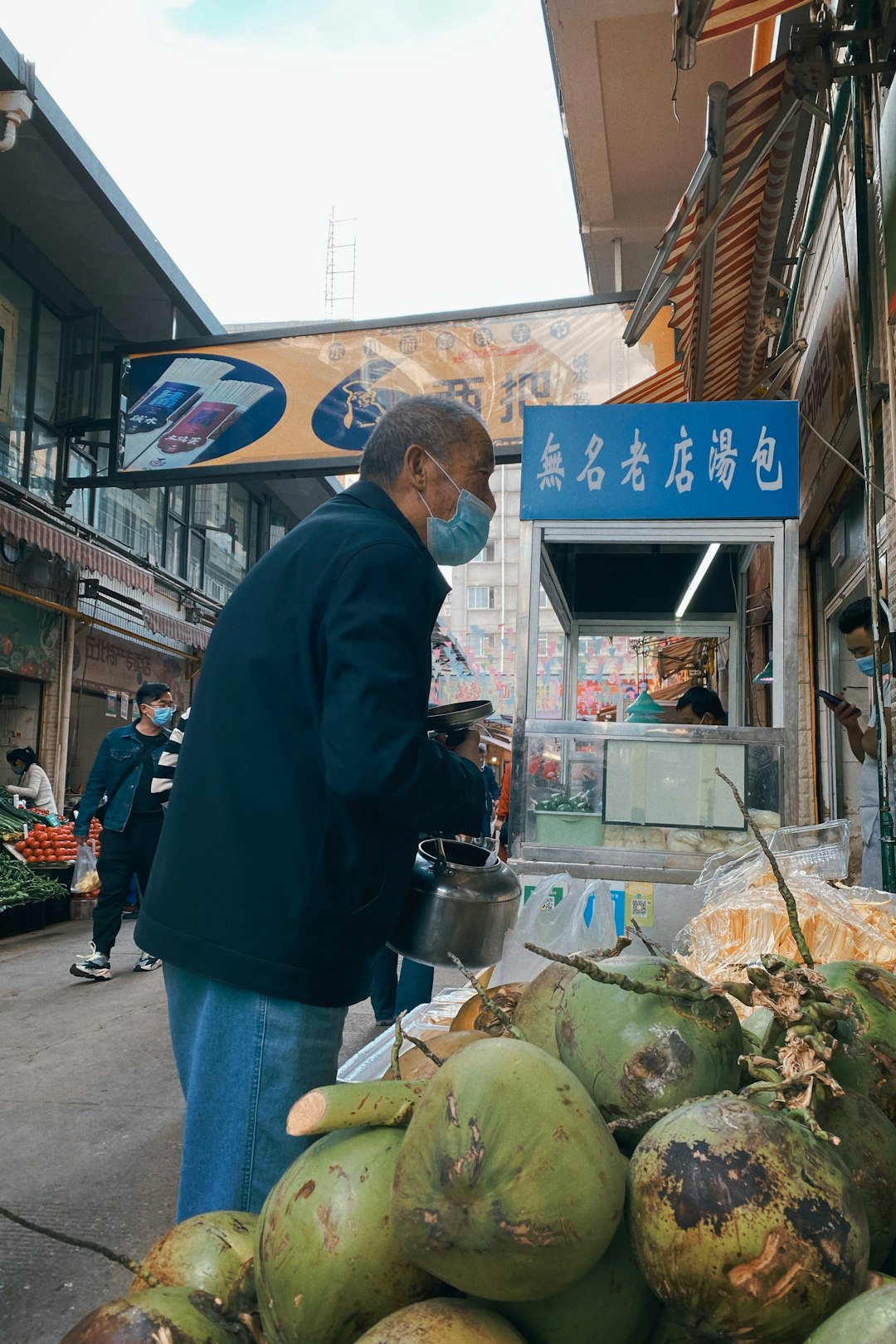 man in blue long sleeve shirt and blue denim jeans standing in front of food stall