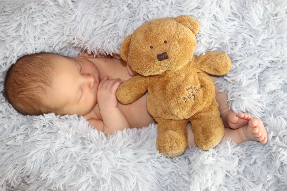 baby lying on white fur textile beside brown bear plush toy