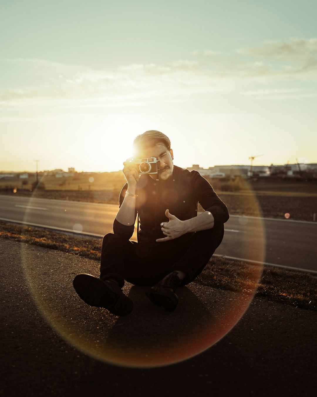woman in black jacket sitting on road during sunset