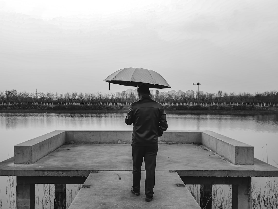 man in black jacket and pants holding umbrella standing on dock during daytime