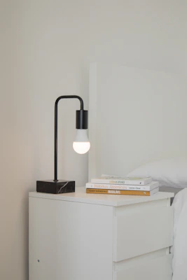 A bedside setup with a compact nordlys side table holding a small lamp and a stack of books.