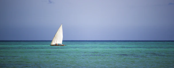 A sailboat cutting through turquoise Mediterranean waters under a bright blue sky.