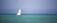 A luxurious sailboat gliding through calm ocean waters under a clear blue sky.