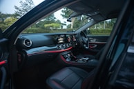 The image depicts the interior of a luxury car, featuring a sleek, modern dashboard with illuminated displays and ambient lighting. The black leather seats complement the high-tech controls and touchscreen interface.
